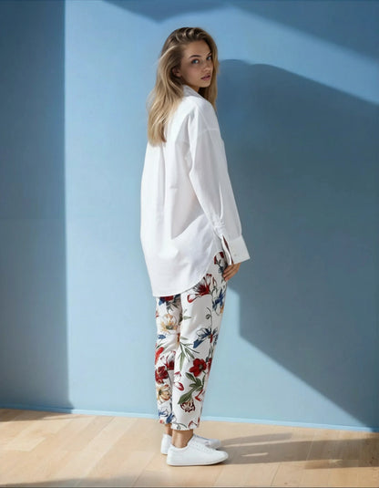 Femme portant une chemise blanche et un pantalon fleuri, pose tendance sur fond bleu, 974 Réunion